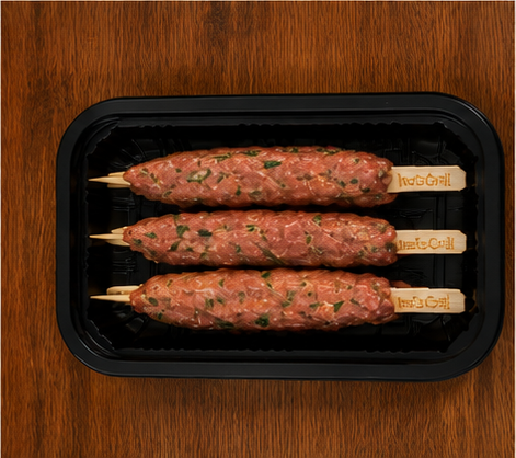Three uncooked kebabs on sticks in a black plastic tray on a wooden surface.