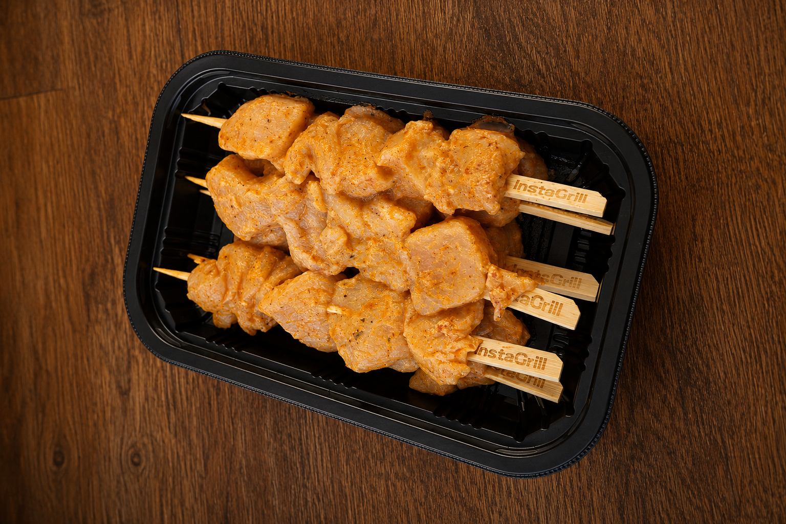 Plastic tray with chicken skewers on a wooden surface