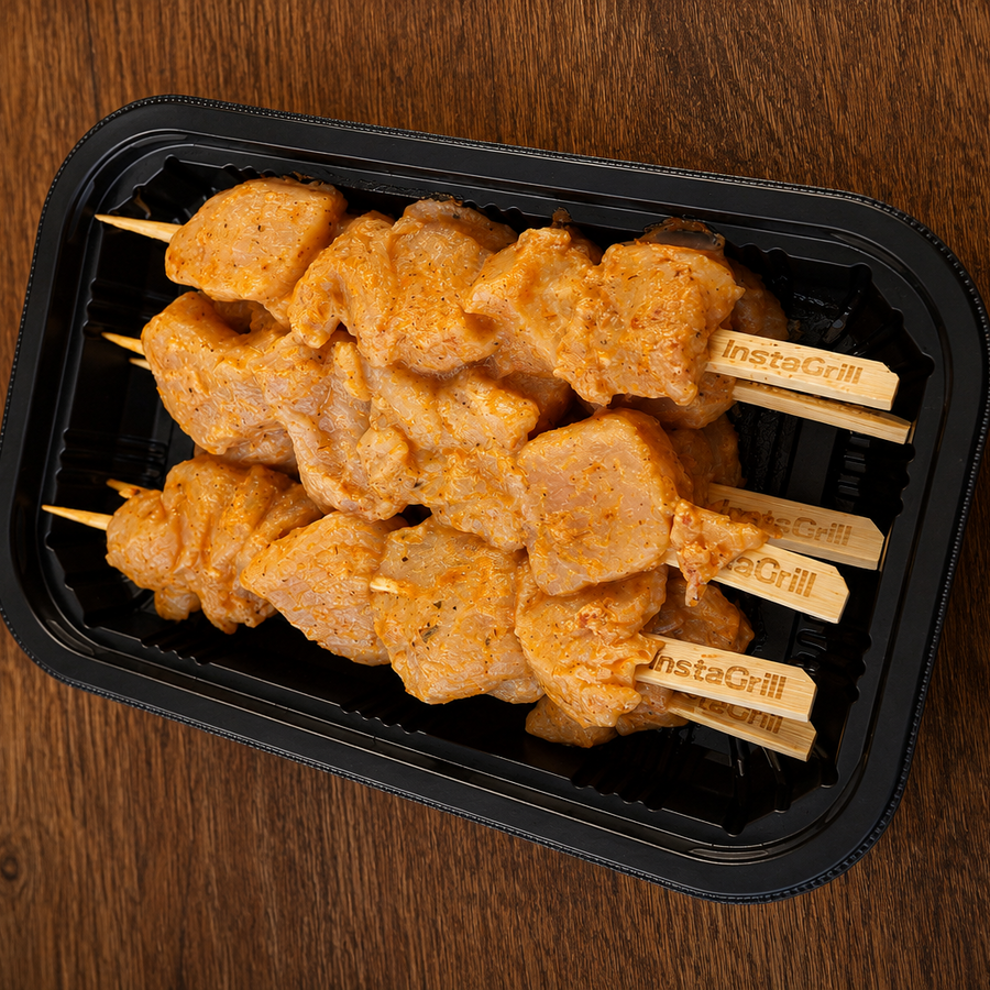 Plastic tray with chicken skewers on a wooden surface